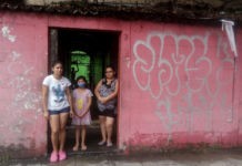 Jennifer Maldonado (I), su hermanita y Carmen Carbajal, a la entrada de su vivienda, en San Salvador. Ellas colgaron una bandera blanca como señal de que se habían quedado sin alimentos durante la cuarentena adoptada por el gobierno desde el 21 de marzo para contener los contagios de la covid-19, como hicieron muchas otras familias en El Salvador y en la vecina Guatemala. Foto: Edgardo Ayala/IPS