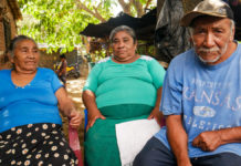 María del Carmen Lipe (I), junto a su hija y su esposo, en el patio de su casa, en el cantón La Guacamaya, del municipio de Nahuizalco, en el oeste de El Salvador, recordando las historias que le contaba su padre sobre la matanza de indígenas y campesinos en 1932. © Edgardo Ayala / IPS