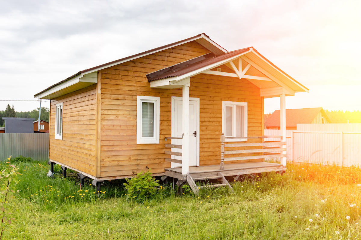 small-tiny-wooden-frame-house-with-sundeck-and-white-windows-and-door-as-a-country-residence-in-sunny-summer-day Casas prefabricadas, precios para considerar