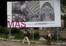 Dos hombres caminan en el céntrico barrio de Vedado, en La Habana, junto a un cartel de la Campaña “Eres más”, por la no violencia hacia las mujeres. © Jorge Luis Baños / IPS