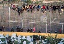 Migrantes encaramados a la valla de Ceuta vigilados por la Guardia Civil.